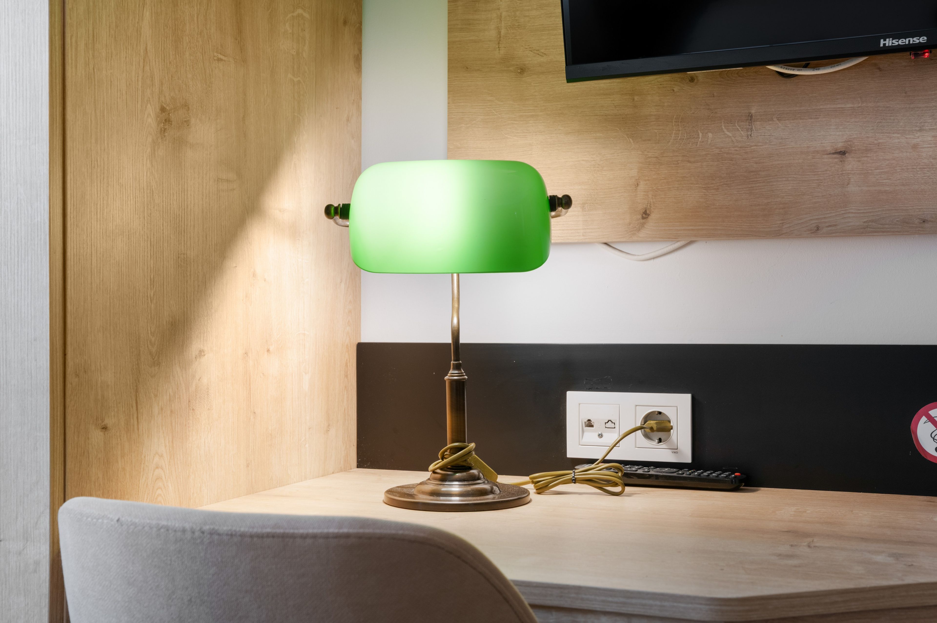 A desk with a green desk lamp, a remote control, and a power outlet with a cable plugged in.
