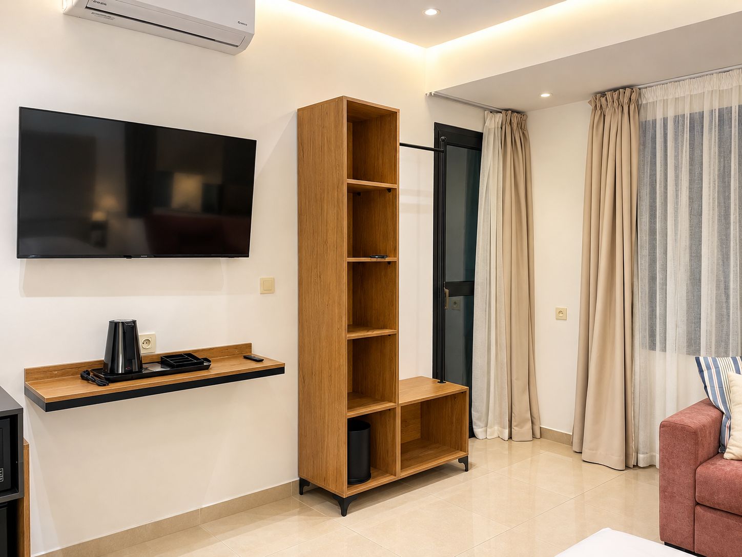 A modern living room with a flat-screen TV, a wooden bookshelf, a coffee machine, and a red sofa.
