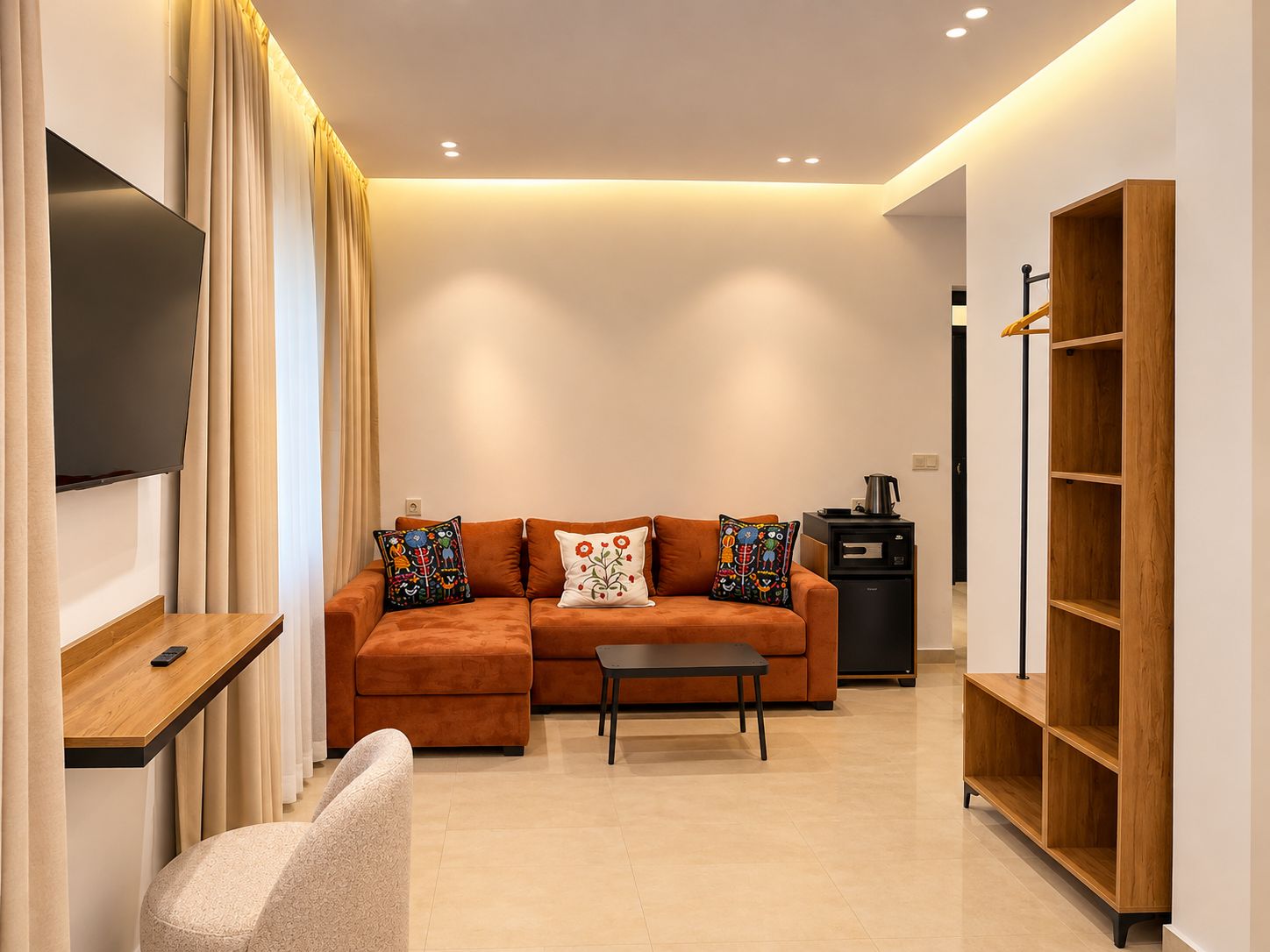 A modern living room with a sofa, a coffee table, a TV, a bookshelf, and a small kitchen area.