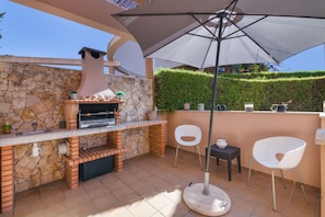 An outdoor patio with a stone wall, a grill, two white chairs, and a table. - Holiday Home 'Villa Quarto Crescente' with Shared Pool, Private Terrace and Air Conditioning (Albufeira)