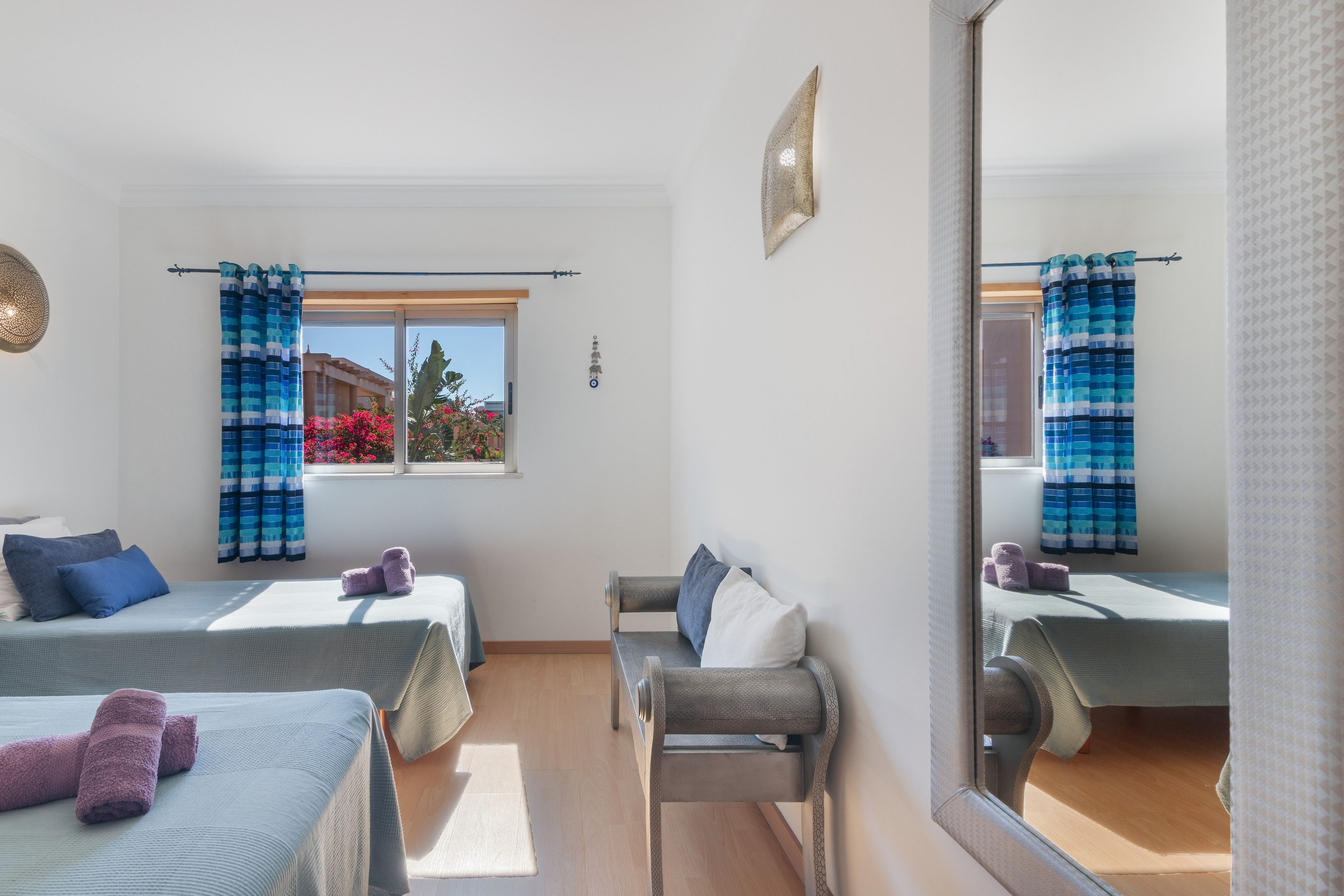 Une chambre avec deux lits, une chaise, une fenêtre avec des rideaux et un miroir.