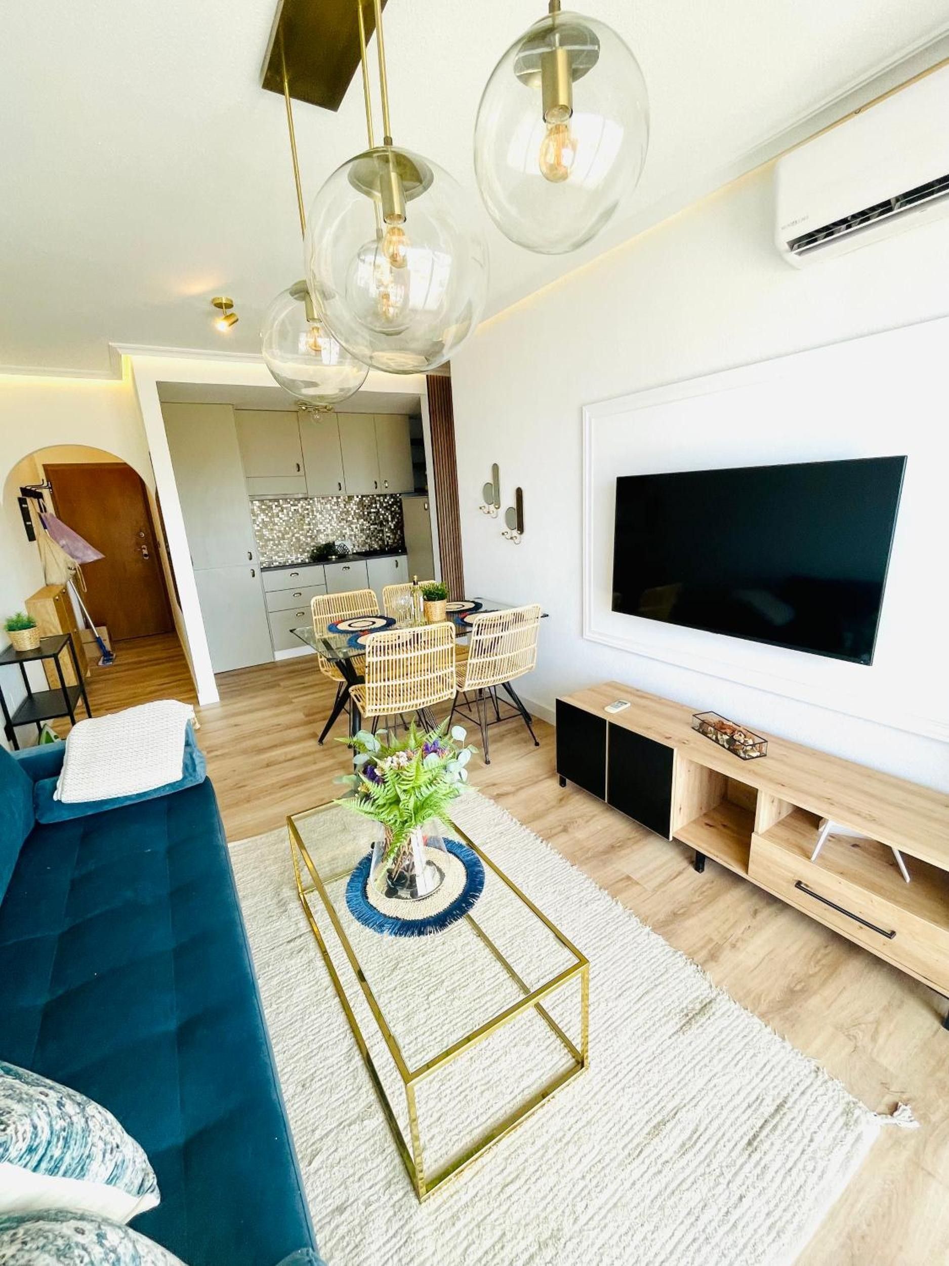 Un salon moderne avec un canapé bleu, une table basse surmontée d’un vase, un téléviseur à écran plat et, au fond, une cuisine.