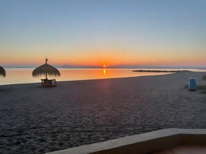 Une scène de plage avec un coucher de soleil, une hutte à toit de chaume et une poubelle.