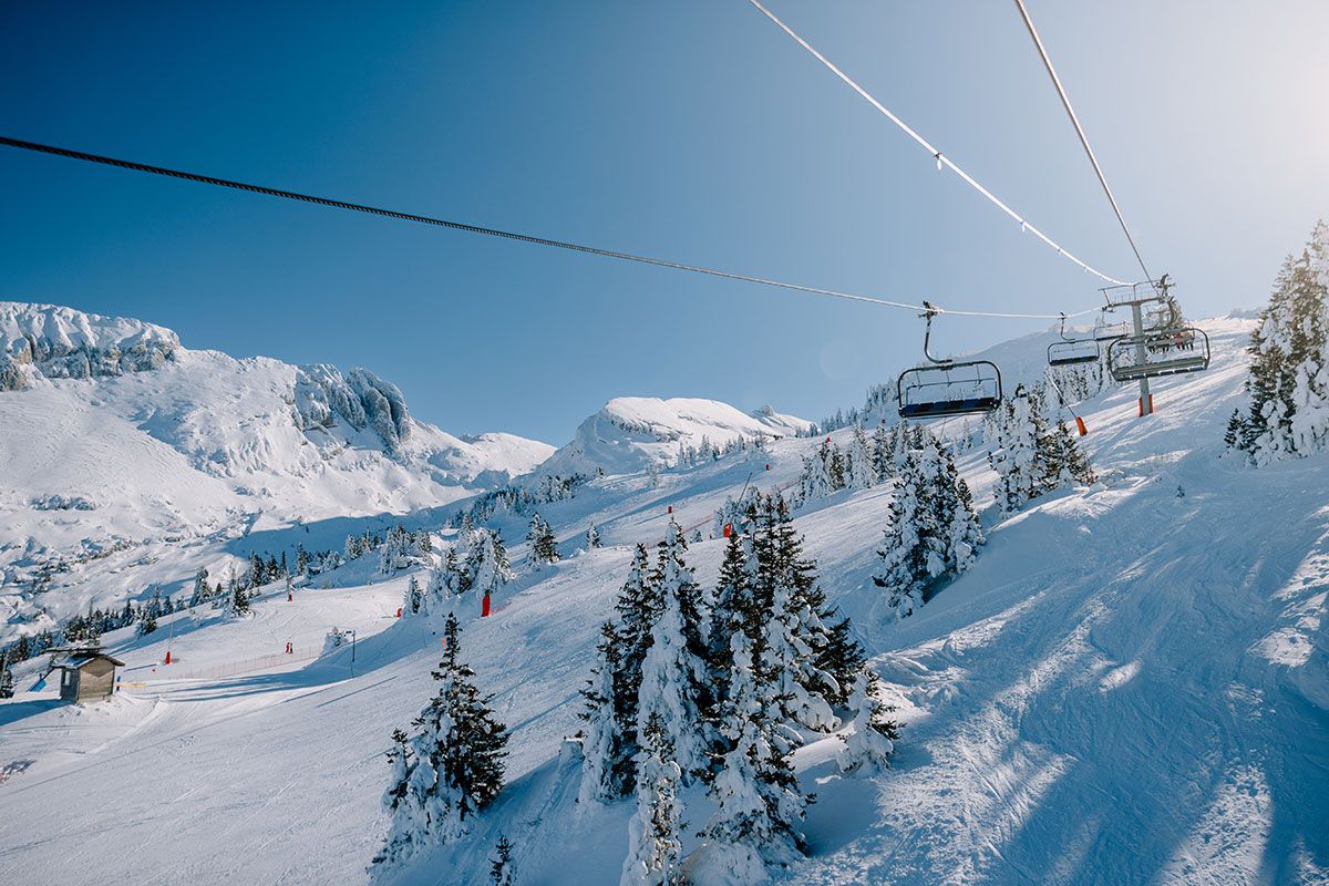 A ski lift with chairs moving up a snowy mountain slope.