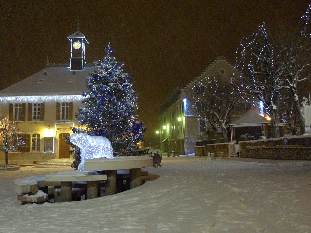 Une place enneigée, avec un sapin de Noël et des structures illuminées.