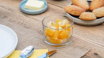 Una mesa de madera con alimentos, incluyendo un vaso de fruta, recipientes pequeños con condimentos y pasteles.