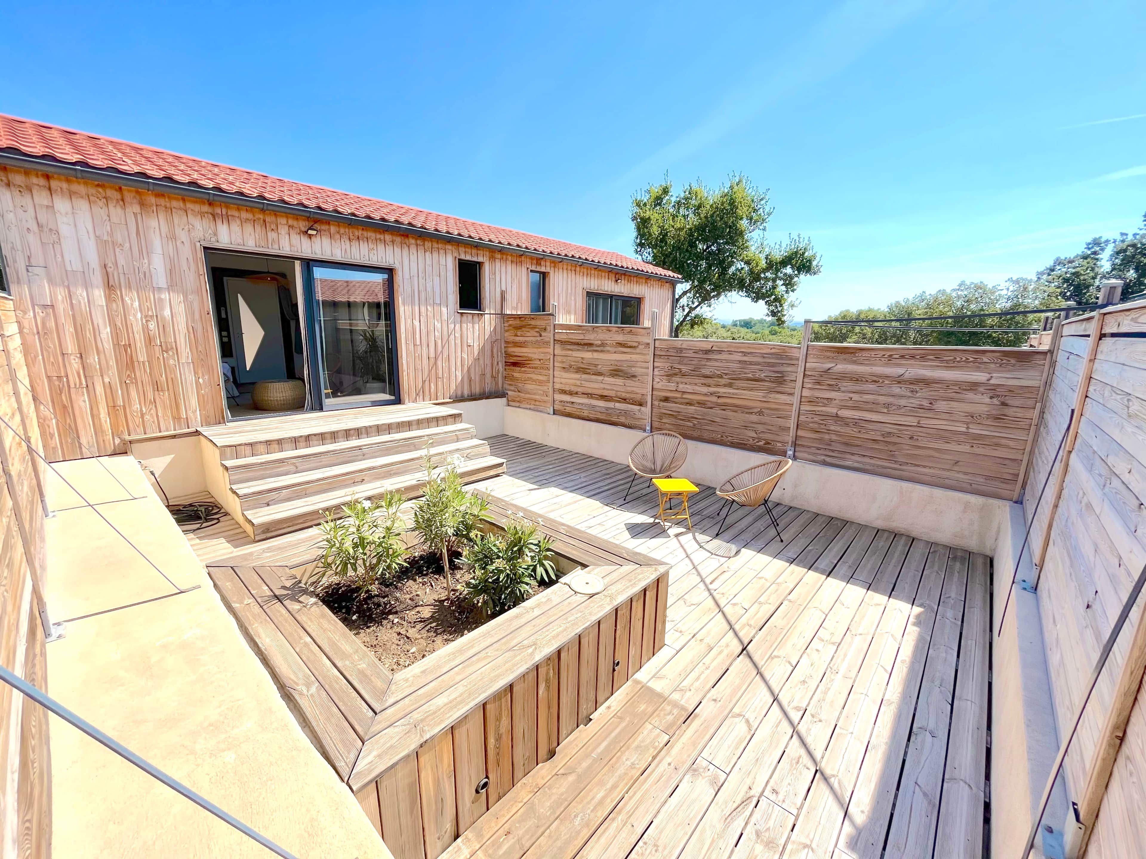 Una terraza de madera con una jardinera integrada, una mesita y dos sillas.