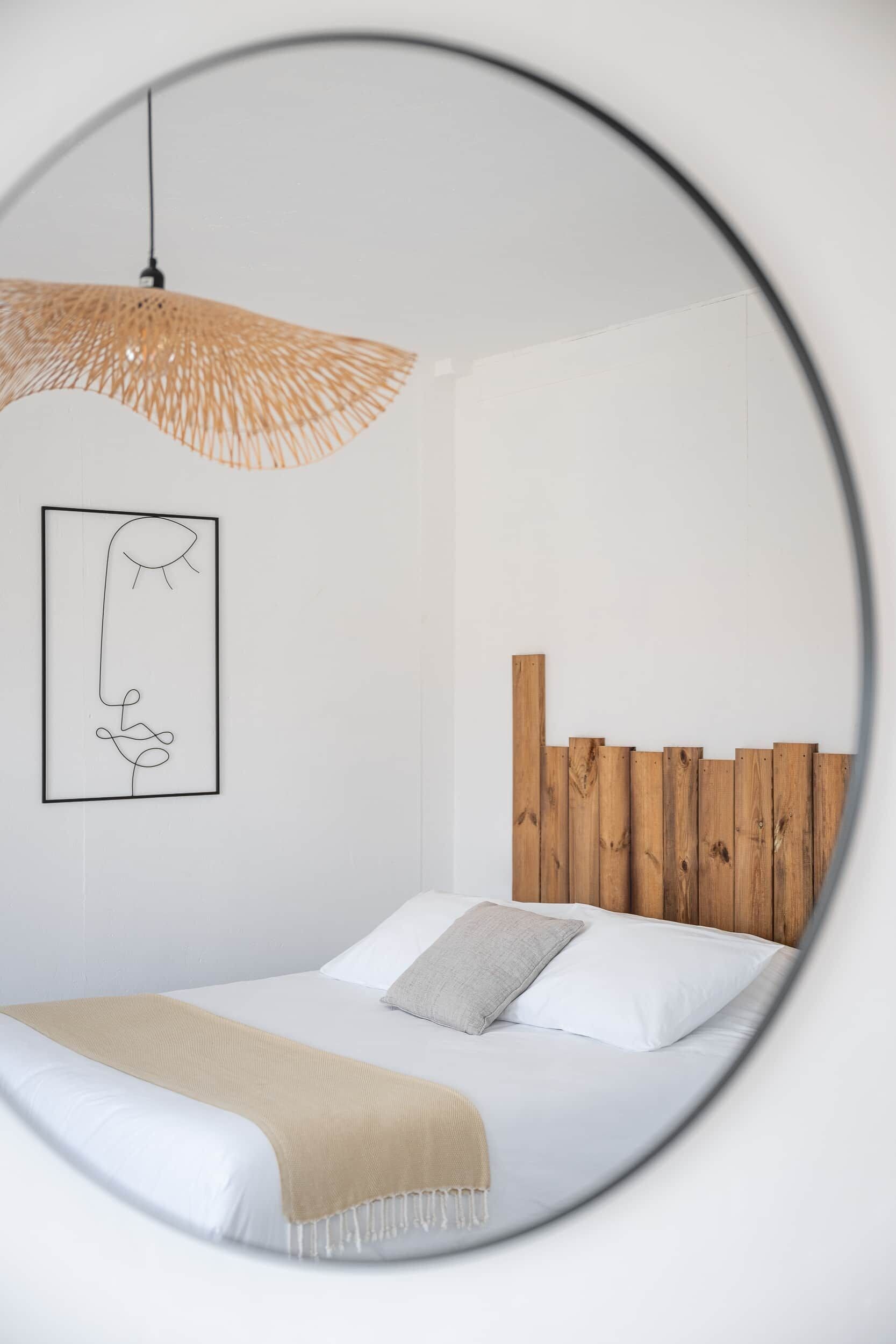 Ein Schlafzimmer mit einem Bett, einer Pendelleuchte, einem hölzernen Kopfteil und einem gerahmten Kunstwerk an der Wand.
