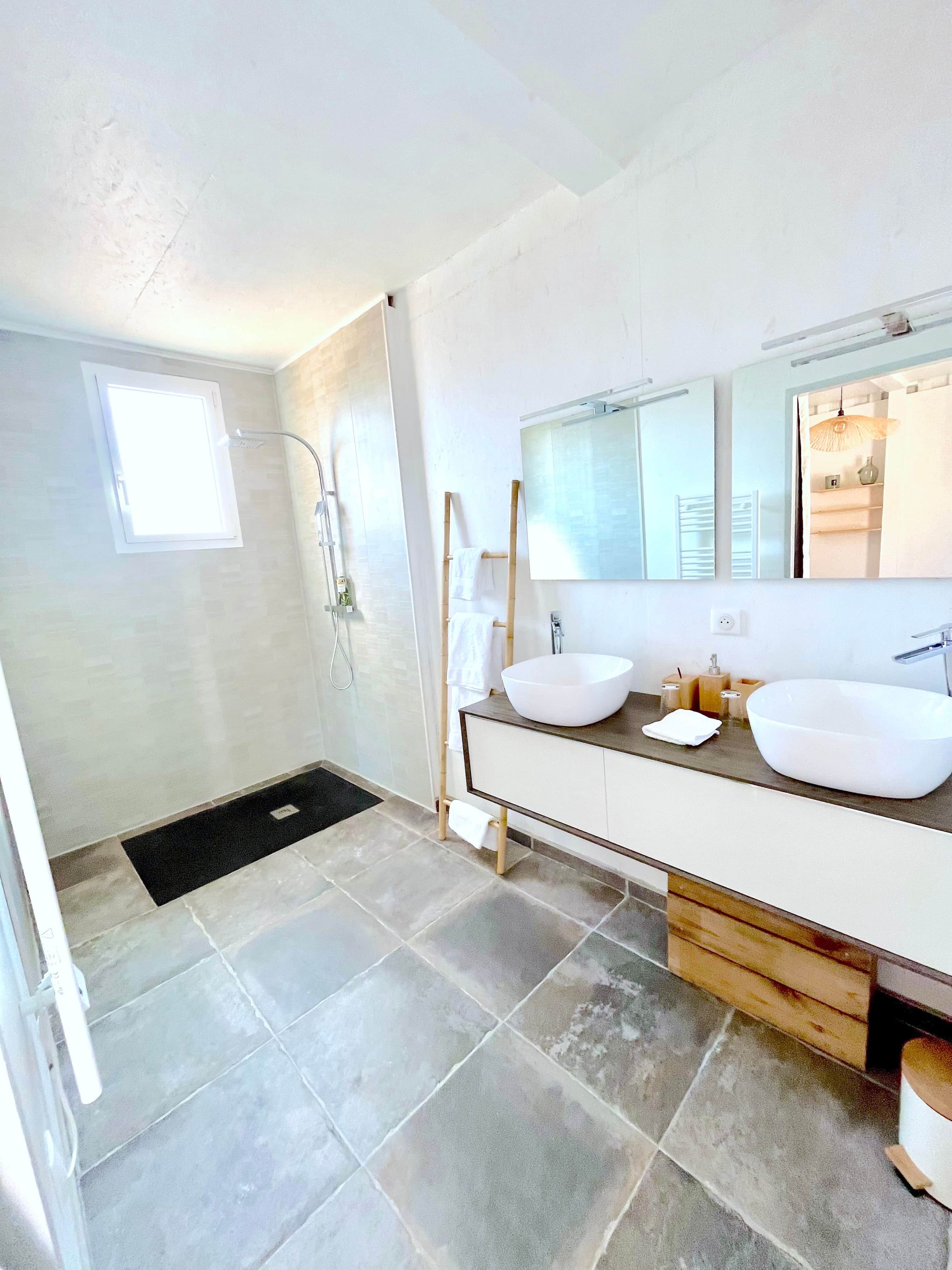 Ein modernes Badezimmer mit zwei Waschbecken, einem großen Spiegel und einer begehbaren Dusche.