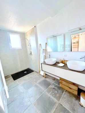 A modern bathroom with two sinks, a large mirror, and a walk-in shower.