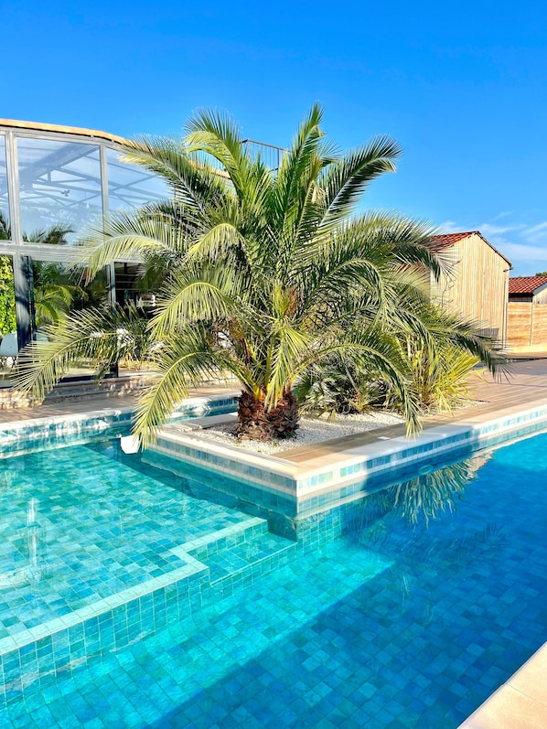 A swimming pool with clear blue water, surrounded by palm trees and a wooden building.