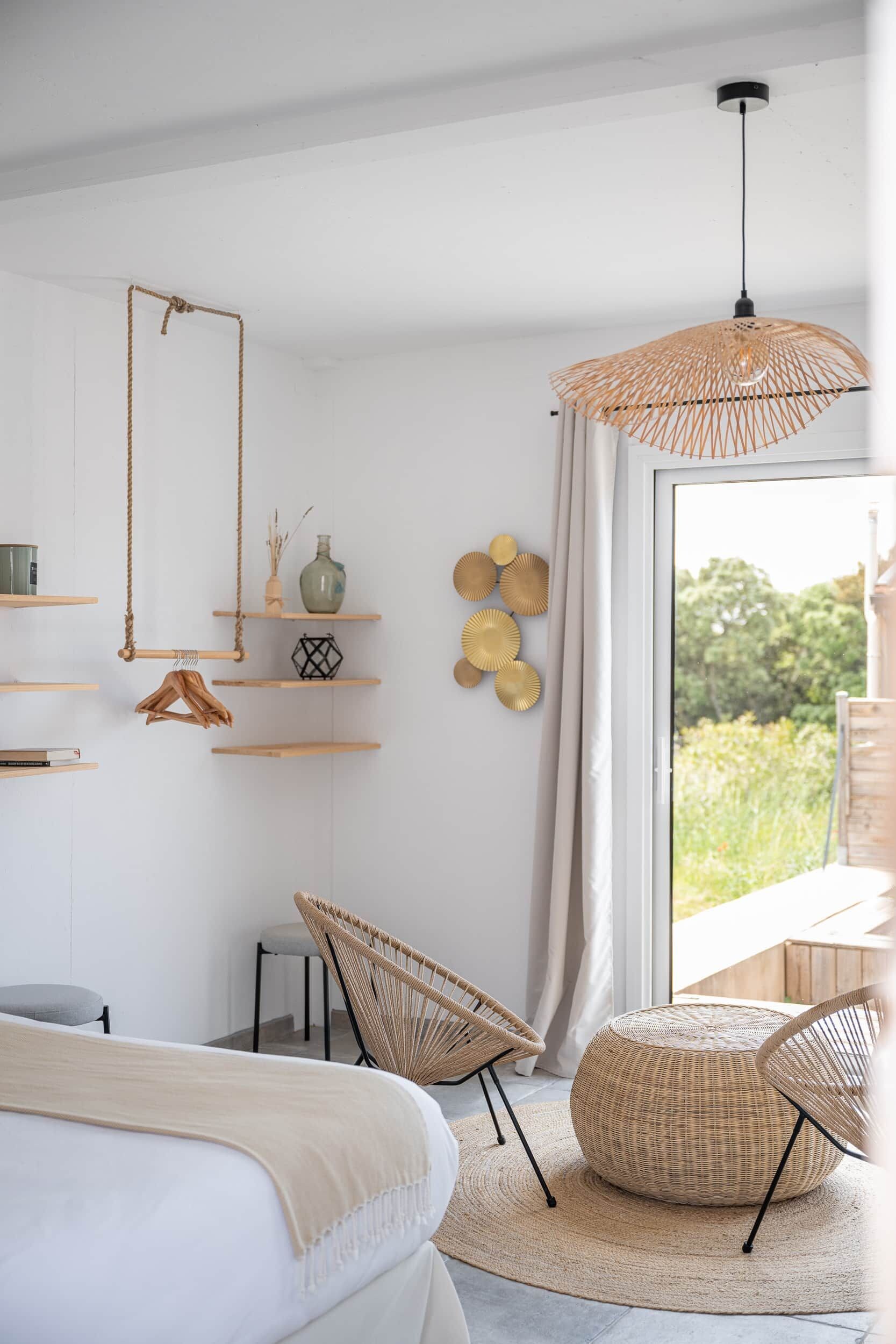 Un dormitorio moderno con una cama, dos sillas de mimbre, una lámpara colgante y vistas al verde exterior.