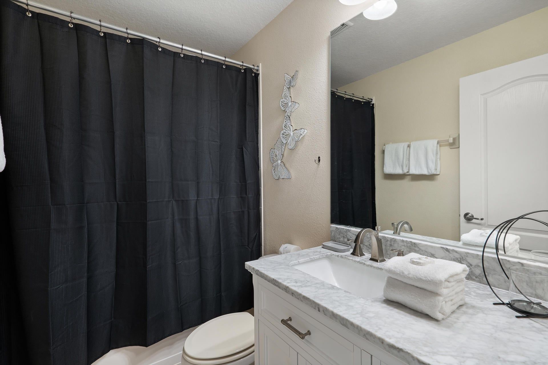 A bathroom with a shower curtain, a toilet, a sink with a marble countertop, and a mirror.