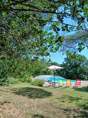 Un giardino con piscina, zona relax coperta e prato.