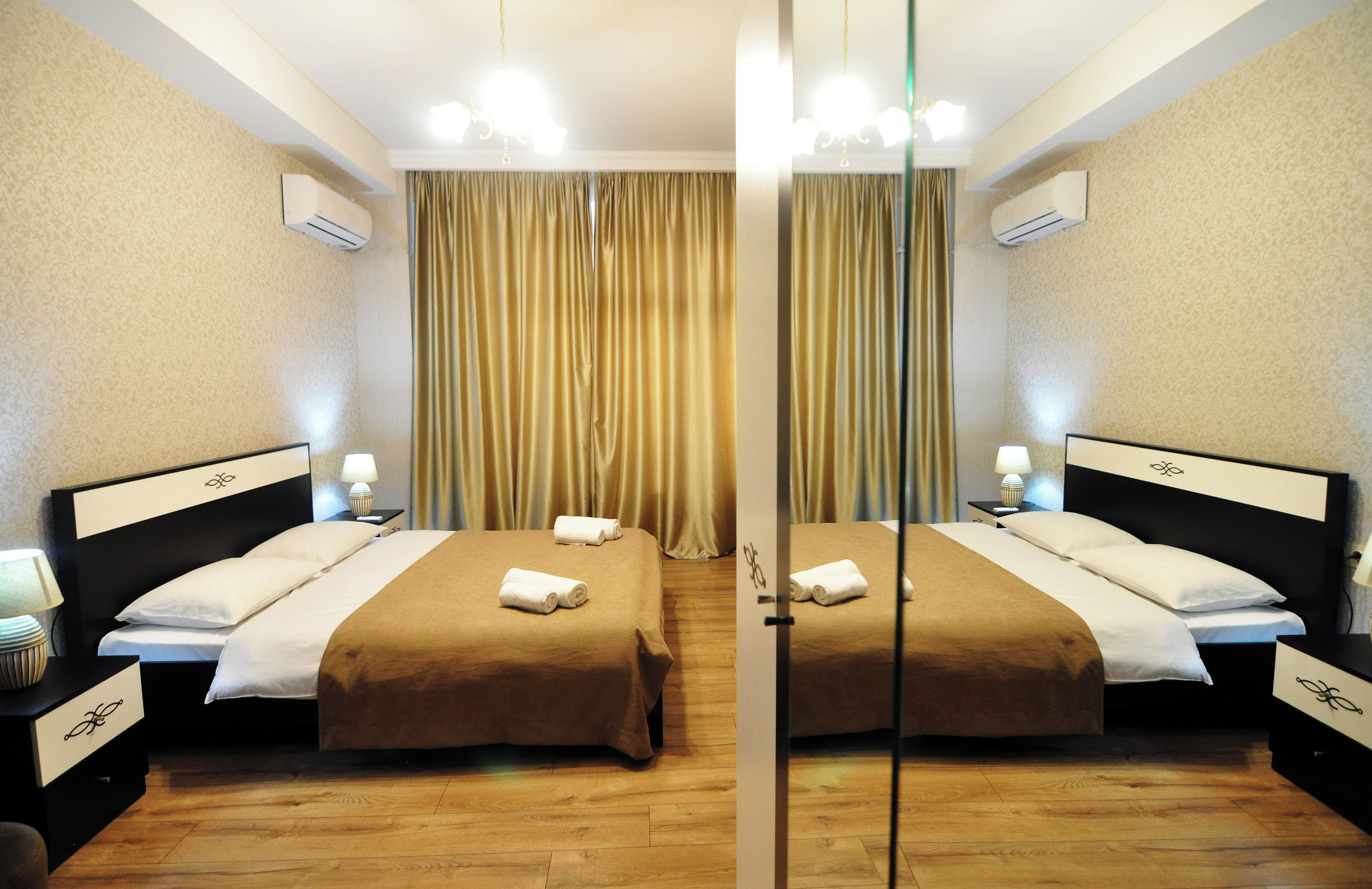 A mirrored hotel room with two beds, wooden flooring, and a curtain divider.