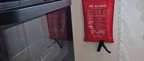 A kitchen with a stove, oven, and a fire blanket hanging on the wall.