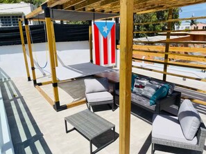 A rooftop patio with a pergola, outdoor seating, and a flag. - Bucketlist Private Beach Villa Walk Beach-2ndFloor (San Juan)