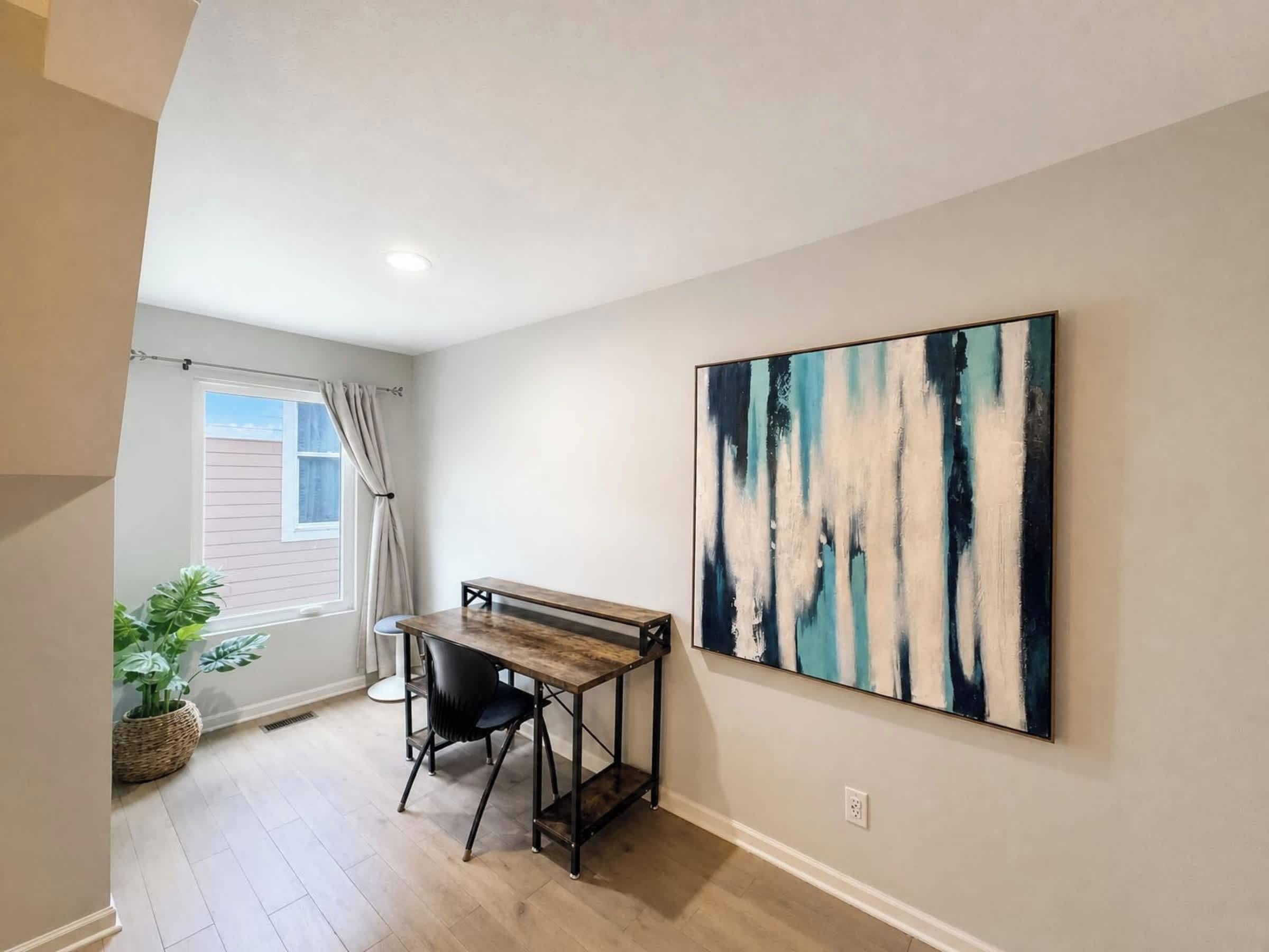 A room with a desk, chair, and a large abstract painting on the wall.