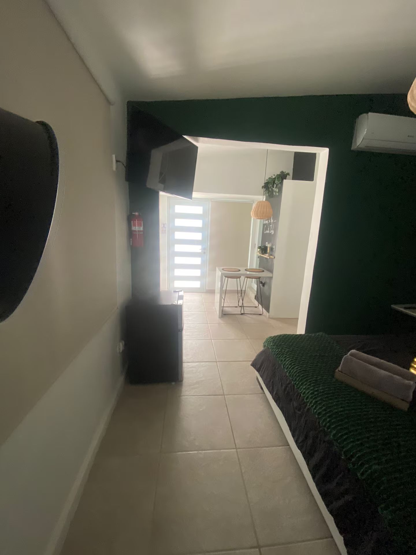 Een kamer met een bed, een klein keukenhoekje en een deur naar een andere kamer.