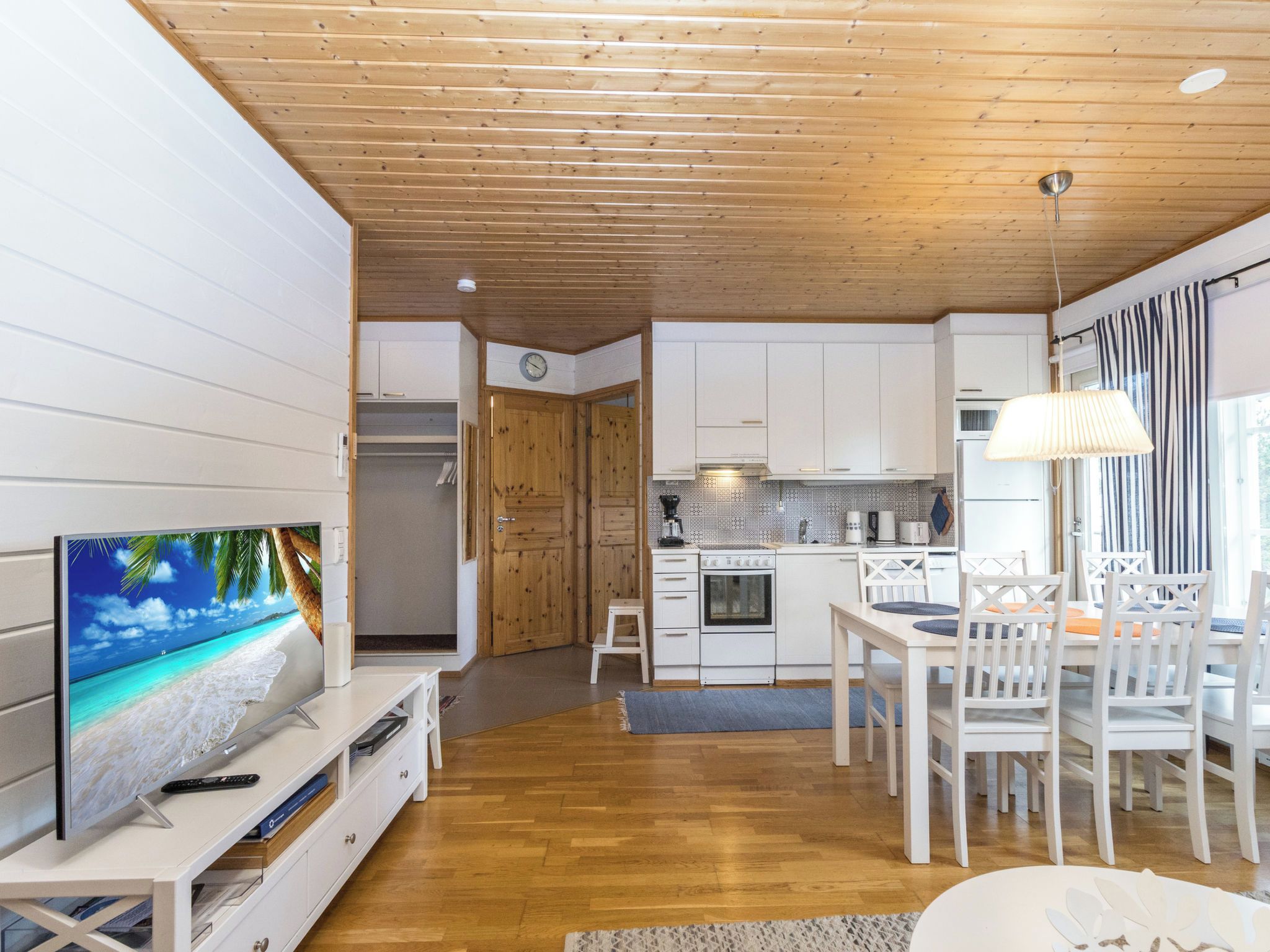 Una cocina moderna con armarios blancos, techo de madera y un comedor con sillas y una mesa blancos.