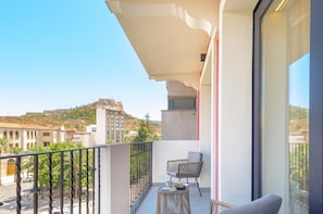 Un balcón con vistas a una colina y edificios, una silla y una mesa con objetos encima.