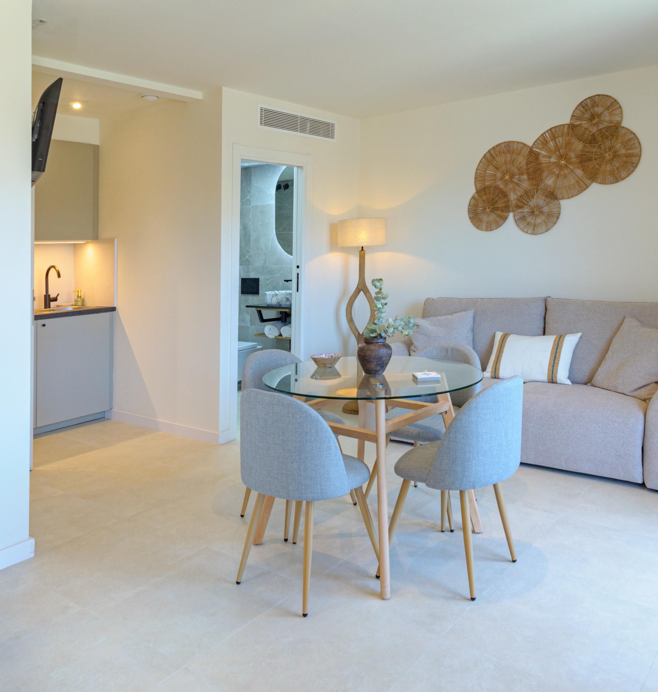 Una sala de estar moderna con una mesa de comedor de vidrio, sillas tapizadas en gris, un sofá color crema y un adorno montado en la pared.