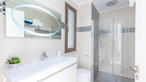 Casa de banho moderna com cabine de duche em vidro, lavatório branco e espelho com moldura decorativa.