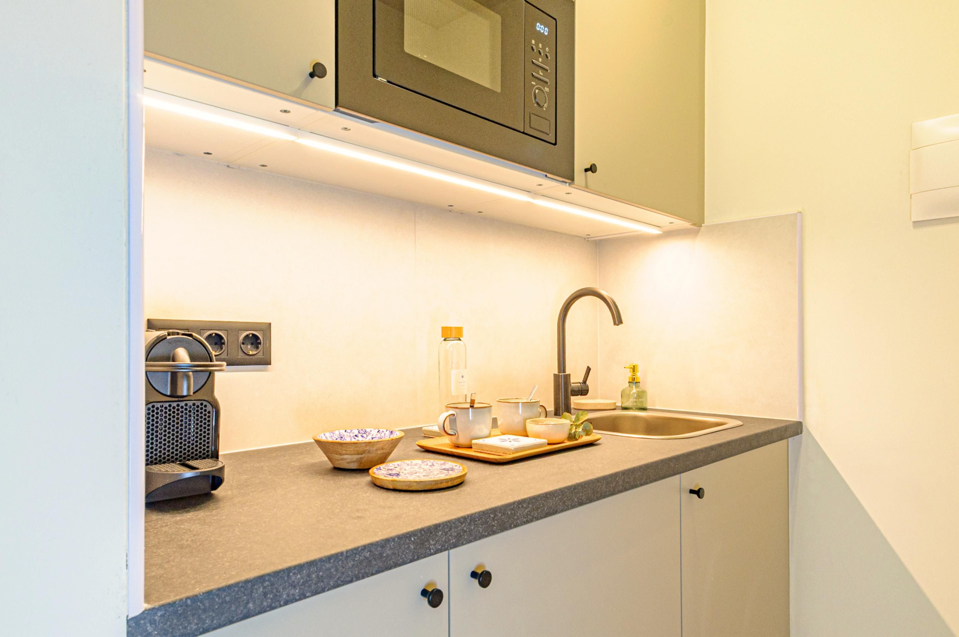 A kitchen with a microwave, coffee maker, sink, and various bowls and cups on the counter.