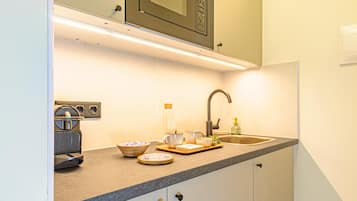 A kitchen with a microwave, coffee maker, sink, and various bowls and cups on the counter.