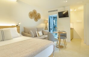 Ein modernes Hotelzimmer mit einem großen Bett, einer Couch, einem kleinen Tisch mit Stuhl, einem an der Wand montierten Fernseher und einem durchgegangenen Tür erkennbaren Badezimmer.