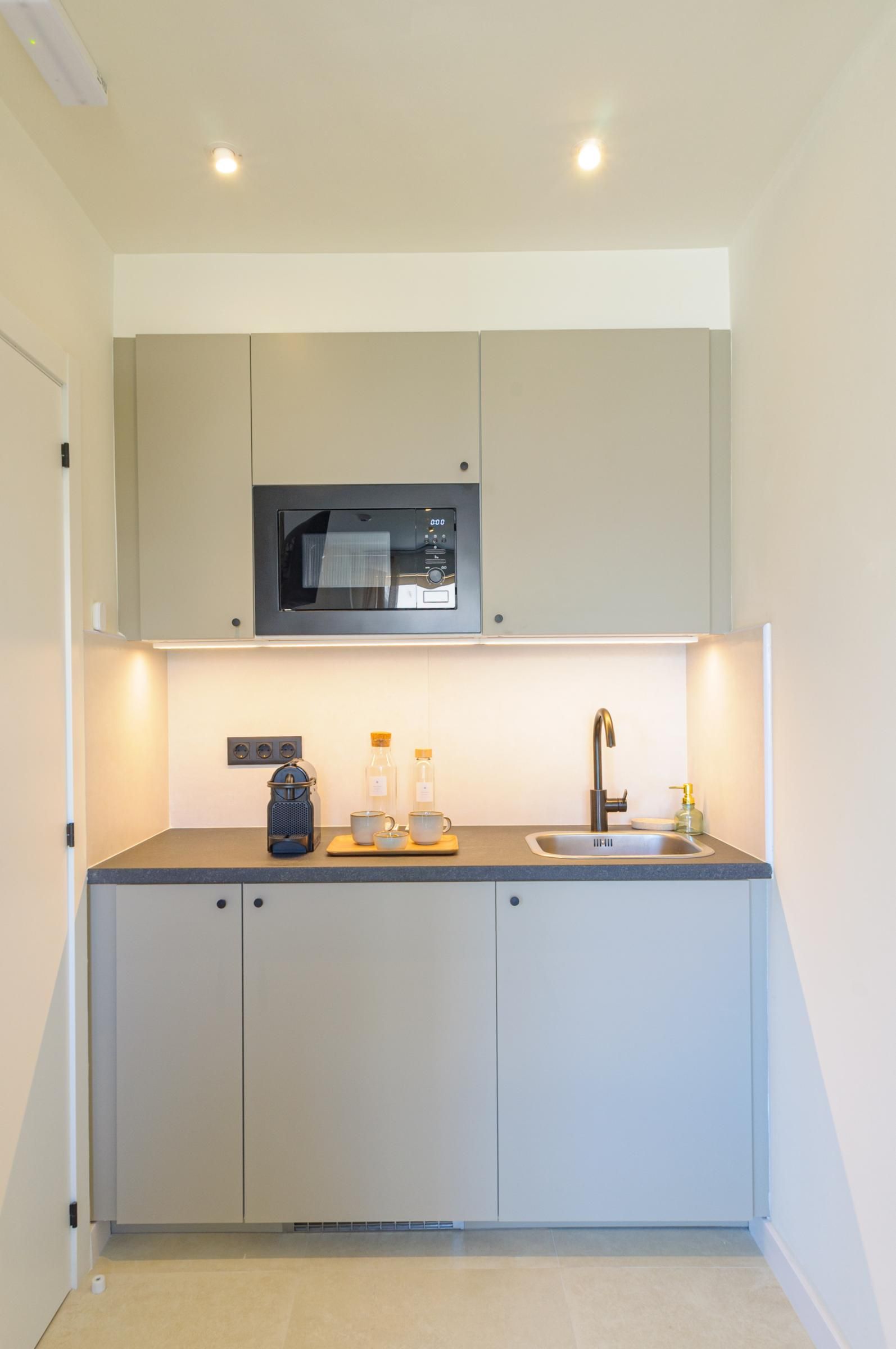 A compact kitchen with a microwave, sink, and a coffee maker.