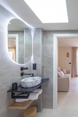 Un baño moderno con lavamanos de mármol, un espejo grande y un perchero para toallas.