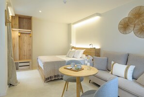 Ein modernes Hotelzimmer mit Bett, Sofa, rundem Holztisch und Wandlampe.