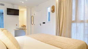 Una habitació d'hotel amb un llit, una televisió penjada a la paret, un escriptori amb una cadira i una finestra amb cortines.