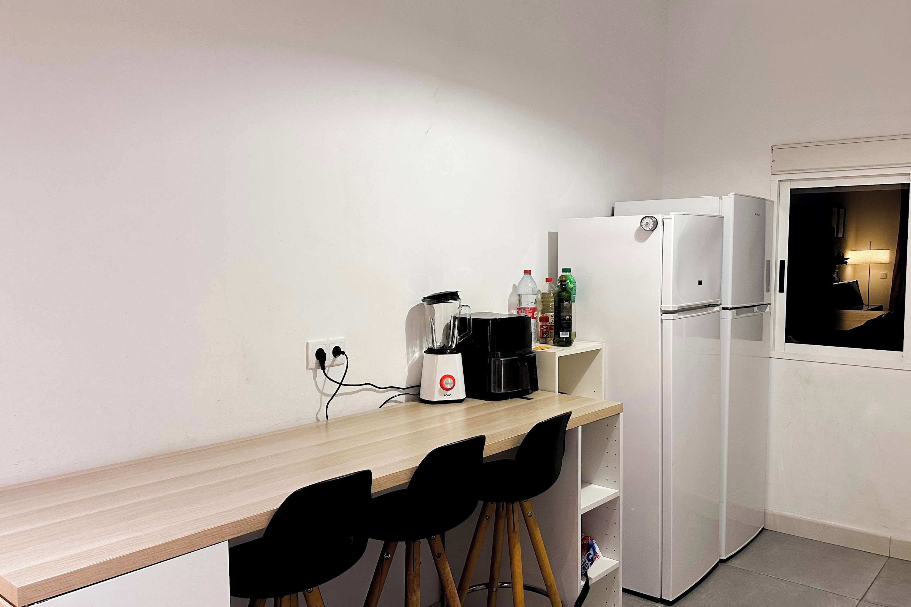Una kitchenette compacta con una encimera, cafetera, refrigerador y una silla.