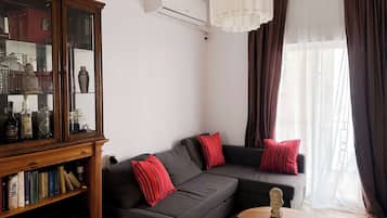 Un salón con un sofá gris oscuro, almohadas rojas a rayas, un aparador de madera con puertas de cristal y una pequeña mesa redonda con una escultura de busto.