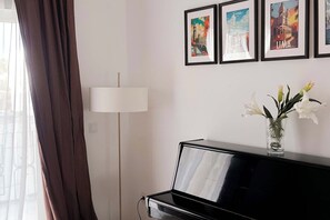 Een kamer met een piano, een lamp en foto’s in lijsten aan de muur.