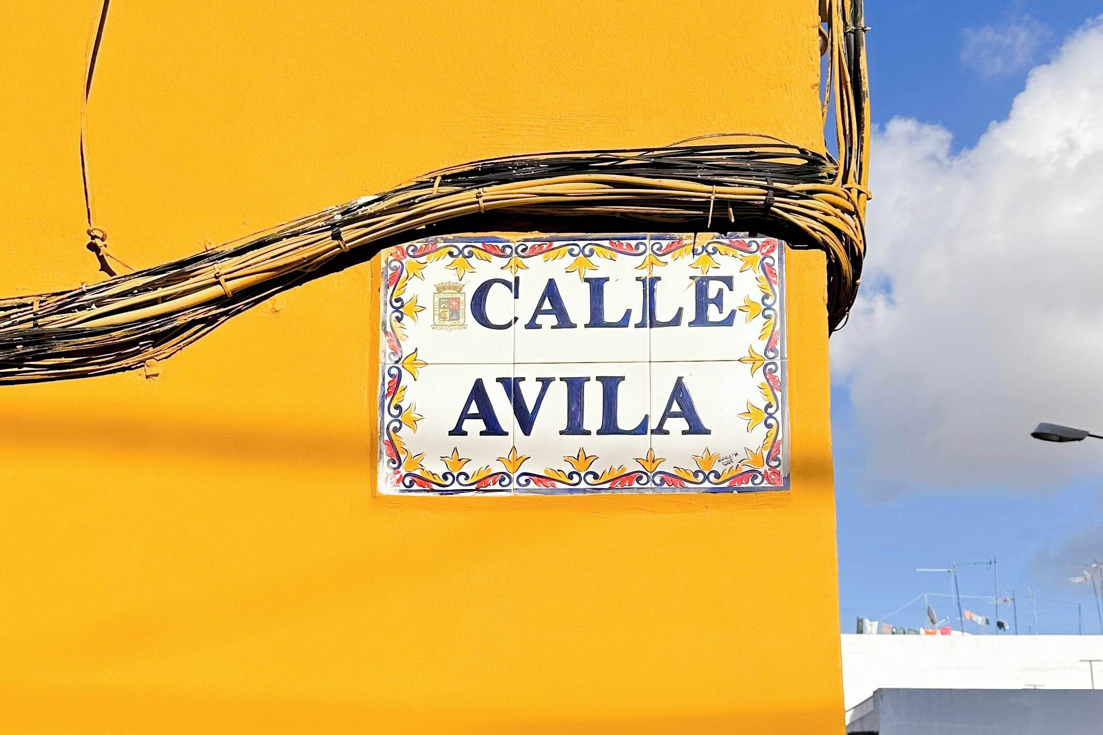 Una señal de calle con la leyenda 'Calle Avila', adherida a un edificio amarillo.