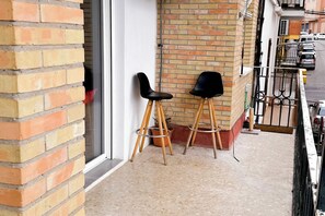 En balkon med to sorte stole, en murstensvæg og gelænder af metal.