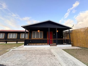 Un edificio con un porche, una puerta roja y una valla.