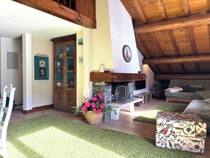 A cozy living room with a stone fireplace, wooden beams, a green carpet, and a sofa. - New Listing (Megève)