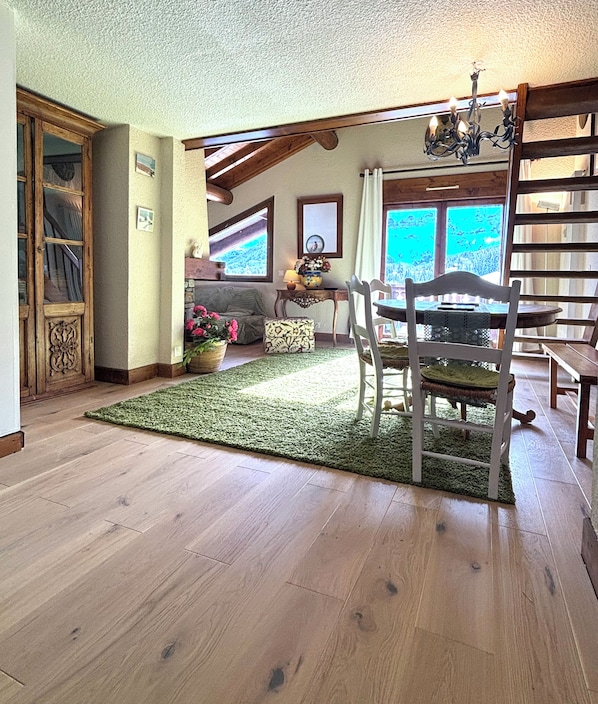 A room with wooden flooring, a dining table with chairs, a chandelier, and a view through a window. - New Listing (Megève)
