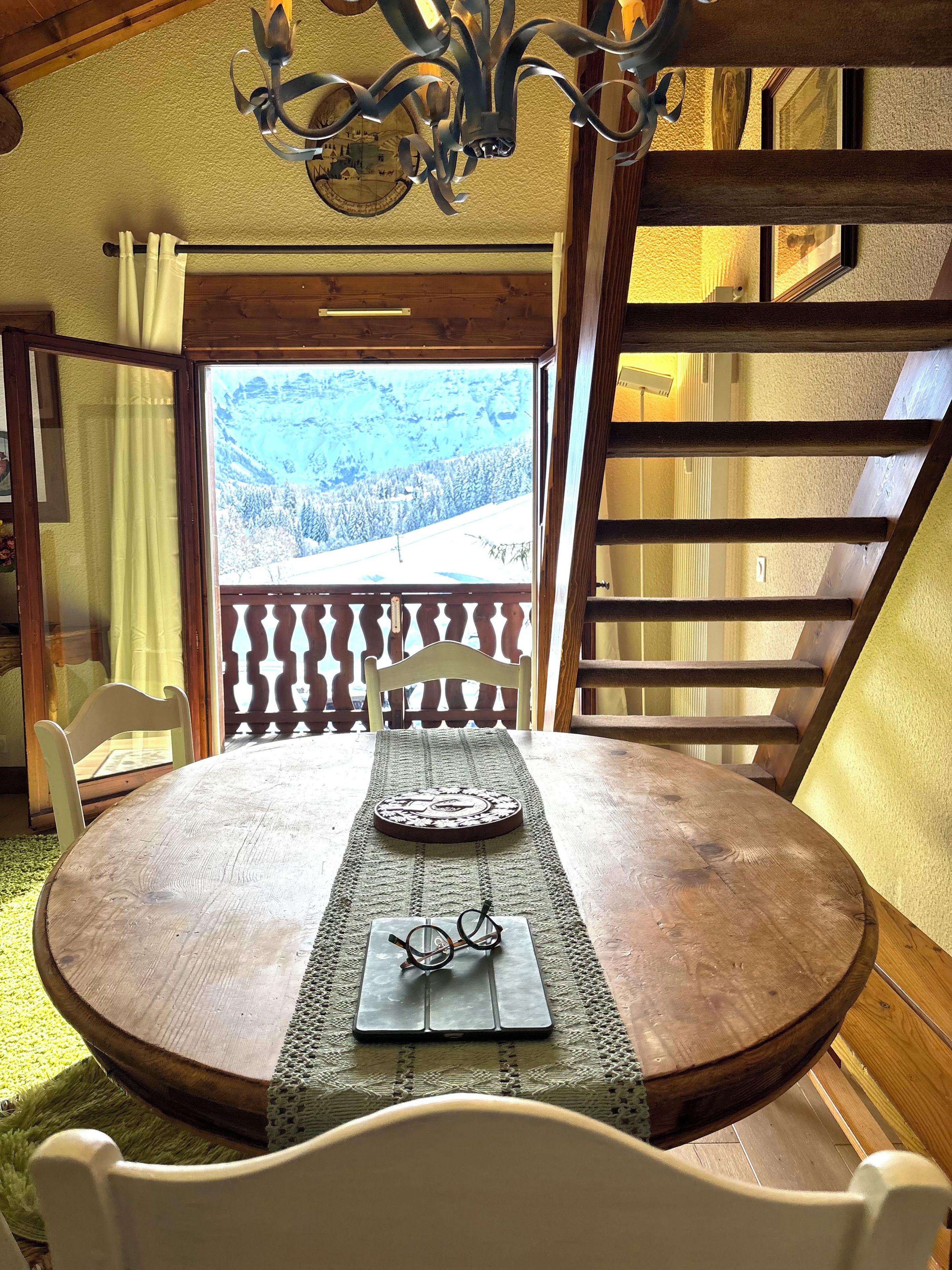 A wooden dining table with a placemat, a pair of glasses, and a decorative plate. A wooden chair is positioned in front of the table.