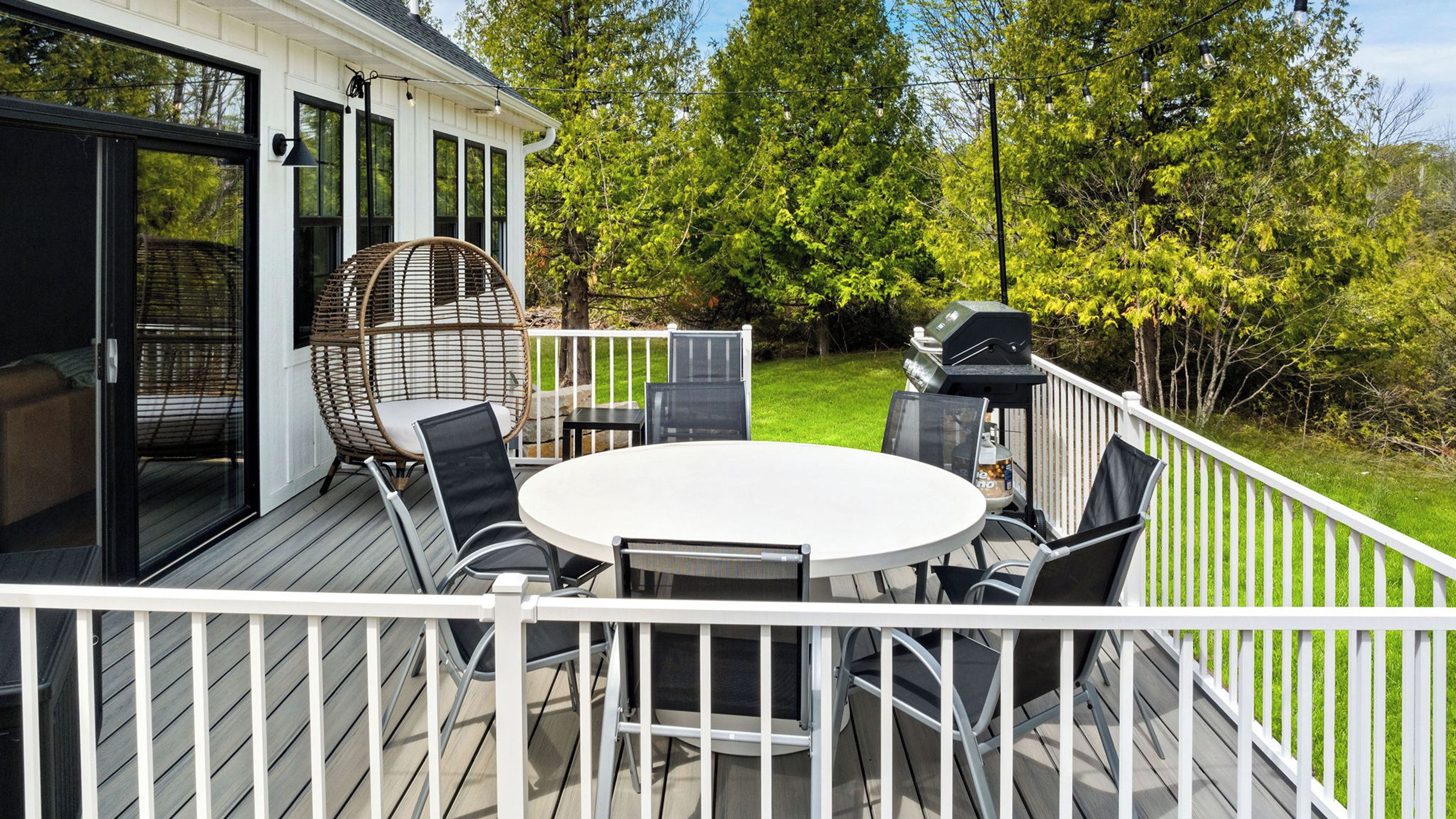 A deck with a round table and chairs, a wicker chair, and a grill.