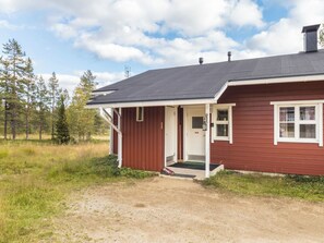 Una casa de madera roja con techo oscuro, un porche y una puerta.