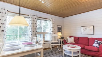 Una habitación acogedora con techo de madera, un sofá rojo, una mesa blanca con individuales y una ventana con cortinas.