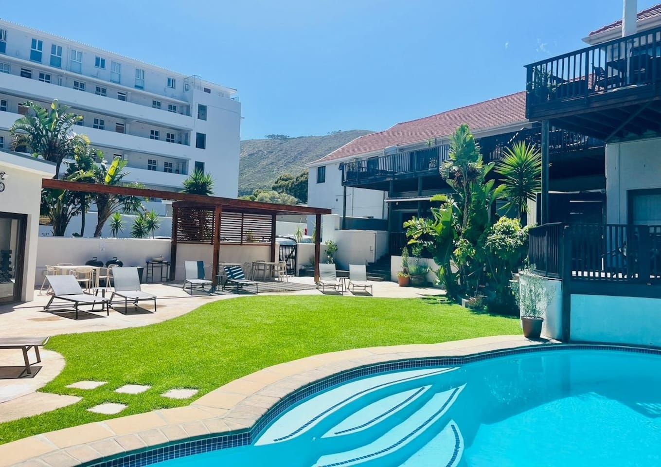 Ein Wohngebiet mit Swimmingpool, einer überdachten Terrasse mit Sitzgelegenheiten und einem gepflegten Rasen.