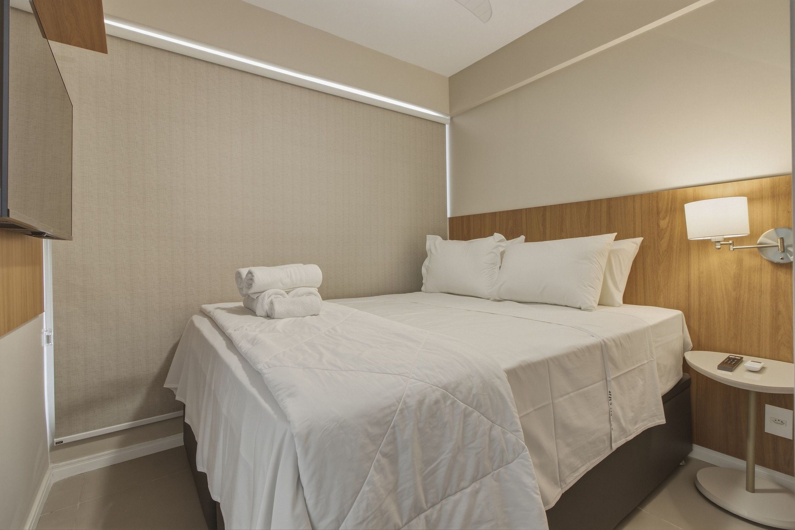 Une chambre d’hôtel avec un lit bien fait, une table de chevet avec une lampe et une petite table ronde avec une télécommande.