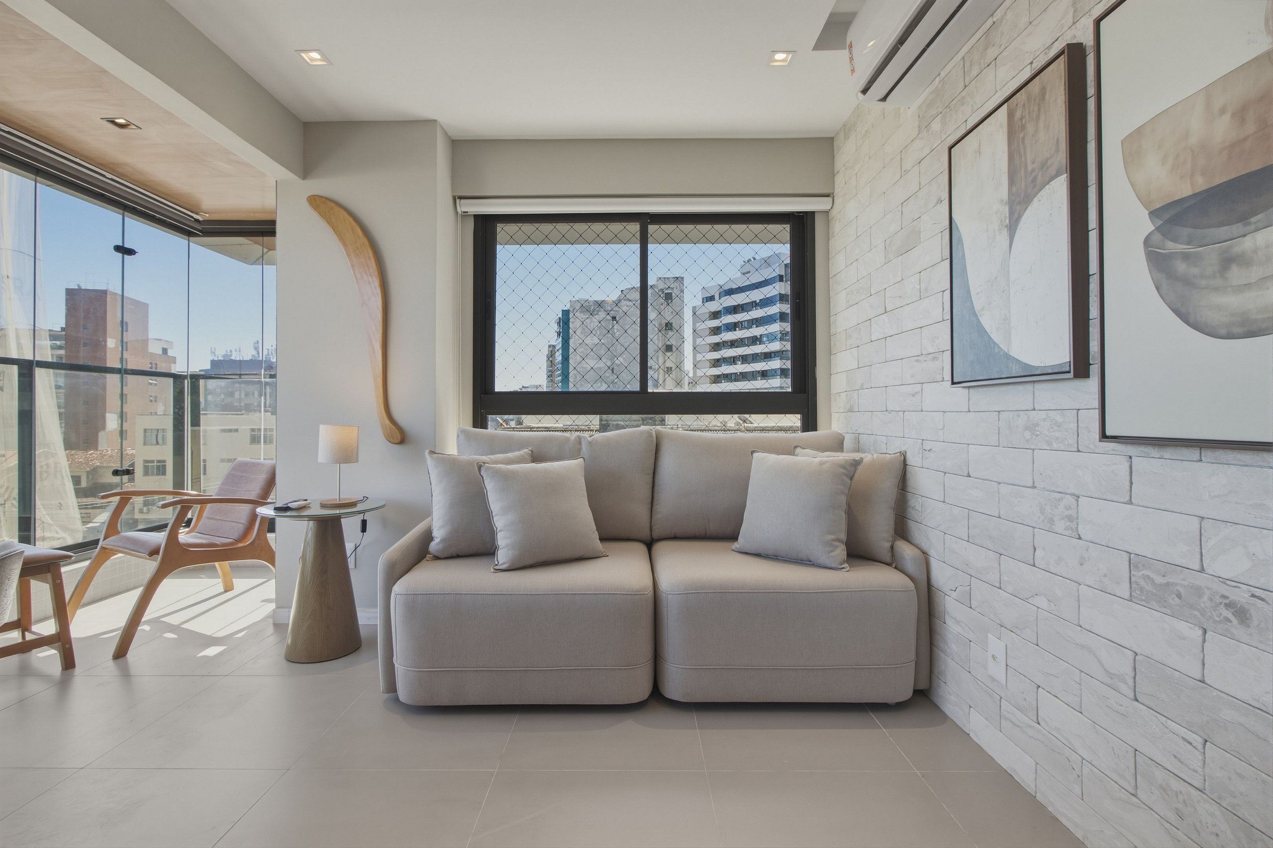 Un salon moderne comprenant un canapé, une table et des chaises, une grande fenêtre donnant sur des immeubles et un mur orné d’un motif texturé.