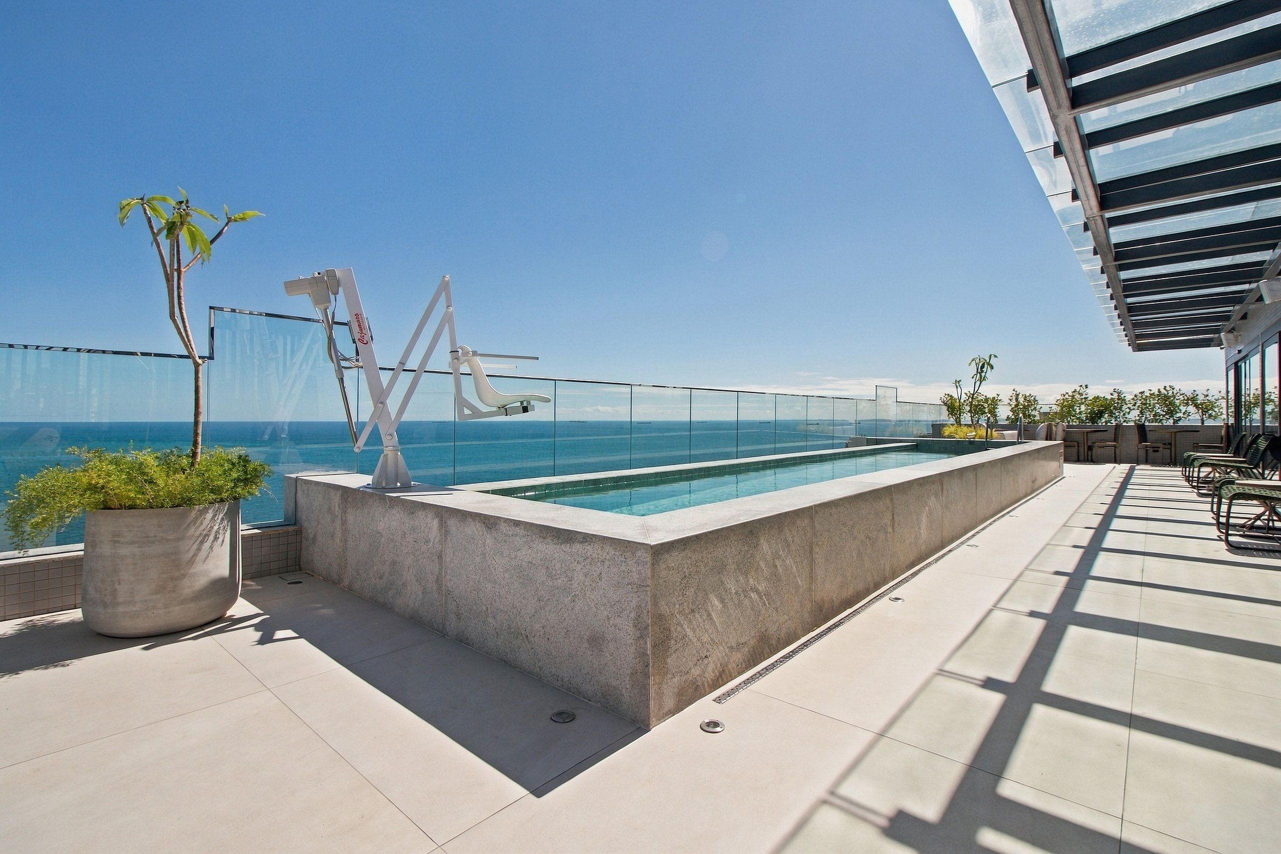 Ein Pool auf dem Dach mit freiem Blick auf das Meer, einer Glasbrüstung und Sitzgelegenheiten im Freien.